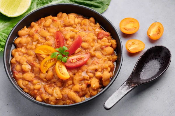 Ful Medames ya da Fava Beans gri arka planda siyah kasede. Foul Mudammas, Mısırlı, Lübnanlı, Suriyeli, Eritre asıllı, İsrail mutfağından pişirilmiş kimyon, domates, maydanoz ve fasulyeli kahvaltı tabağı.