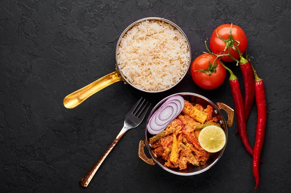 Bakır kadai 'de sebze Jalfrezi ve siyah tahta kaplamalı basmati pilavı. Jalfrezi, Hint mutfağı. Kızarmış sebze ve baharatlı domates sosu. Hint Yemeği.