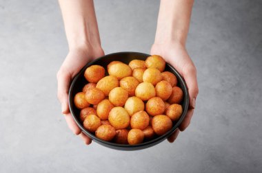Loukoumades ya da Luqaimat ya da Lokma siyah kasede kadının ellerinde gri zeminde. Loukoumades, Ramazan 'da popüler olan bir doğu mutfağı çöreğidir. Popüler Ramazan Yemeği. İftar ve Suhur tatlıları