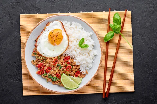 Pad Krapow Gai - Thai Basil Chicken with Rice and fried Egg black slate background. Pad Krapow is Thai cuisine dish with minced chicken or pork meat, basil, soy and oyster sauces. Thai Food.