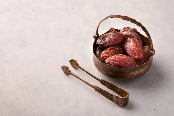 Date Fruits or Kurma in the bronze plate at grey concrete background. Dates and water is Ramadan meal. Ramazan Iftar food. Copy space