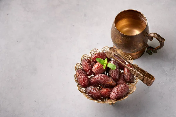 Date Fruits or Kurma in the bronze plate at grey concrete background. Dates and water is Ramadan meal. Ramazan Iftar food. Copy space