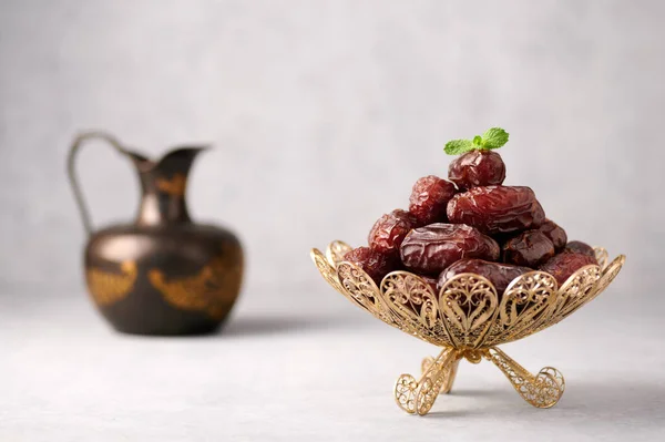 Date Fruits or Kurma in vintage arabic dish and jug of water at grey concrete background. Dates and water is Ramadan meal. Ramazan Iftar food.