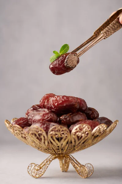 Date Fruits or Kurma in the bronze plate at grey concrete background. Dates and water is Ramadan meal. Ramazan Iftar food.