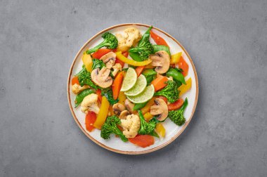 Pad Pak Ruam veya Veg Thai karıştırılmış sebzeler gri beton zeminde beyaz tabakta. Pak Tayland mutfağı ve sebze ve soslu vejetaryen yemeğidir. Tayland yemeği. Uzayı kopyala Üst görünüm