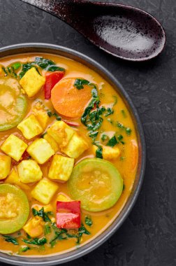 Tofu soslu sarı sebzeli Tayland körisi ve siyah tabakta sebzeler. Tofulu, kabaklı, dolmalık biberli, ıspanaklı, havuçlu vejetaryen Thai Curry. Tayland yemeği. Hint sebzeli köri.