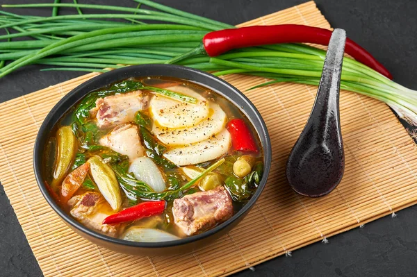 Sinigang na Baboy ya da Filipinli Pork Et Çorbası. Siyah kasede, arka planda. Sinigang, et, bamia, daikon, ıspanak ve balık soslu bir Filipin mutfağıdır. Filipin yemeği. Asya Yemekleri