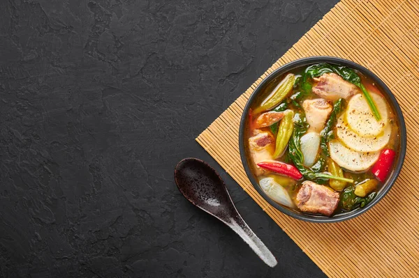 Sinigang na Baboy ya da Filipinli Pork Et Çorbası. Siyah kasede, arka planda. Sinigang - Filipin mutfağı et, bamia, daikon, ıspanak, balık soslu. Filipin yemeği. Asya yemeği. Boşluğu kopyala