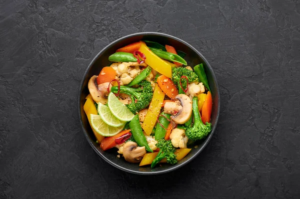 Pad Pak Ruam ya da Veg Thai Kızarmış Sebzeler siyah kasede, arka planda. Pak Tayland mutfağı ve sebze ve soslu vejetaryen yemeğidir. Tayland yemeği. Üst görünüm