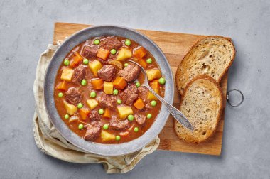 Beton arka planda Matt Gray kasesinde ekmek bulunan İrlanda sığır eti güveci. Sığır etli güveç ya da patates, havuç, bezelye ve otlu kuzu eti. Geleneksel Amerikan ve Avrupa yemekleri. Akşam yemeği.