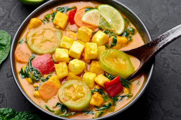 Tofu soslu sarı sebzeli Tayland körisi ve siyah tabakta sebzeler. Tofulu, kabaklı, dolmalık biberli, ıspanaklı, havuçlu vejetaryen Thai Curry. Tayland yemeği. Hint sebzeli köri.