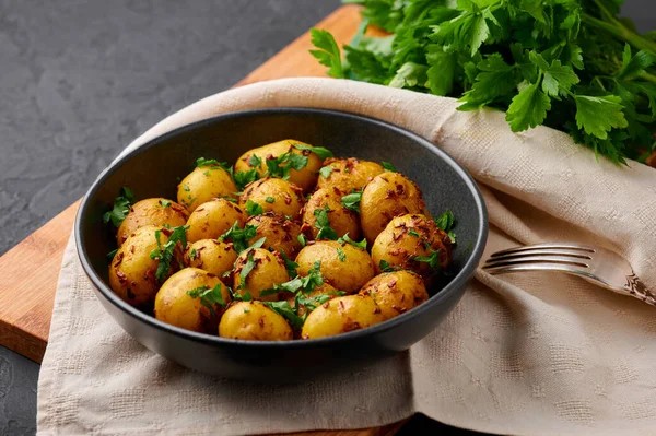 Jeera Aloo in black bowl on dark slate background. Jeera Aloo is indian cuisine dish with little baby potatoes, jeera seeds and coriander. Indian Food.