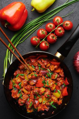 Siyah beton arka planda tavuklu mançurya. Mançuryalı tavuk tavuk tavuk göğsü, dolma biber, domates ve soya soslu Çin mutfağıdır..