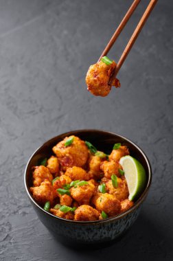 Gobi Mançurya, siyah beton arka planda kasede. Gobi Mançurya, karnabahar, domates, soğan ve soya soslu Hint Çin mutfağı. Boşluğu kopyala