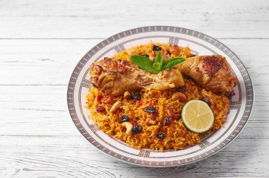 Beyaz ahşap arka planda tavuk kabsa veya tavuk biryani. Kabsa geleneksel Suudi Arabistan mutfağıdır. Kabsa pilavlı, tavuklu, baharatlı, domatesli, fındıklı ve kuru üzümlü yemek yapar.