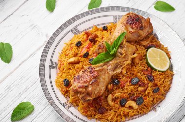 Beyaz ahşap arka planda tavuk kabsa veya tavuk biryani. Kabsa geleneksel Suudi Arabistan mutfağıdır. Kabsa pilavlı, tavuklu, baharatlı, domatesli, fındıklı ve kuru üzümlü yemek yapar.