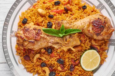 Beyaz ahşap arka planda tavuk kabsa veya tavuk biryani. Kabsa geleneksel Suudi Arabistan mutfağıdır. Kabsa basmati pilavı, tavuk, baharat, domates, fındık ve kuru üzümle pişirir. Kapat.