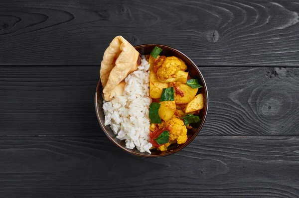 Pilav ve soslu aloo gobi. Hint mutfağı vejetaryen yemeği karnabahar, patates, zencefil, sarımsak ve baharatla pişirilir. Kimyon, kişniş, acı biber ve garam masala. Siyah tahta arkaplan