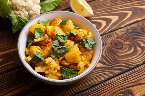 Aloo gobi. Hint mutfağı vejetaryen yemeği karnabahar, patates, zencefil, sarımsak ve baharatla pişirilir. Kimyon, kişniş, acı biber ve garam masala. kahverengi Woden masa üstü