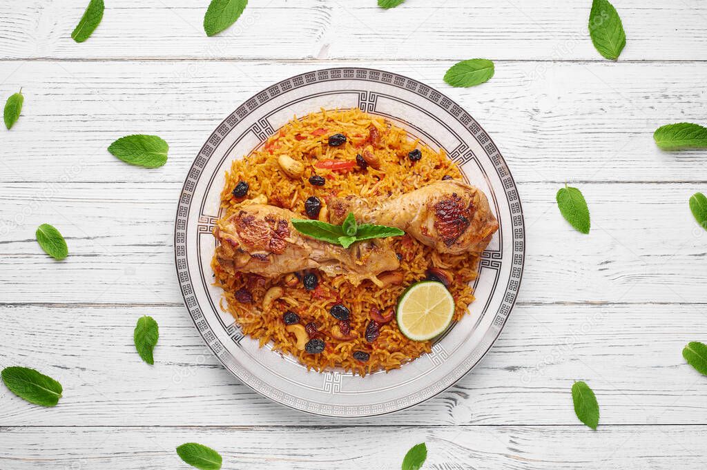 Chicken Kabsa or Chicken biryani at white wooden background. Kabsa is traditional saudi arabian cuisine dish. It cooks with basmati rice, chicken, spices, tomatoes, nuts, raisins. Copy space. Top view