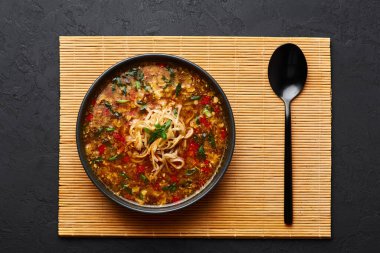 Veg Manchow Çorbası siyah kasede, arka planda. Vejetaryen Manchow Çorbası, Çin mutfağında dolma biber, lahana, havuç, şehriye, kırmızı biber, soya sosu ve yeşil soğan ile servis edilir..