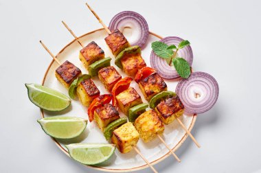 Paneer Tikka, beyaz arka planda izole edilmiş beyaz plakalı şişler içinde. Paneer tikka, içinde sebze ve baharat bulunan ızgara paneer peyniri olan bir Hint mutfağı. Hint yemeği..