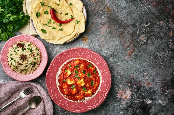 Paneer Makhani, Jeera Rice ve koyu arkaplanda pembe plakalı paratha. Paneer Makhani paneer peyniri, domates ve baharatlı Hint mutfağıdır..