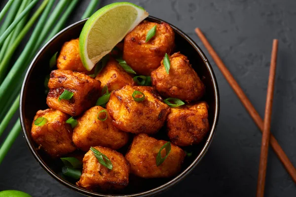 Paneer Mançurya ya da Paneer 65, siyah beton arka planda kasede. Paneer Mançurya, Çin mutfağında panner peyniri, domates, soğan ve soya sosu ile servis edilir. Kapat.