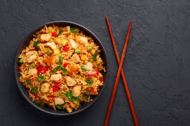 Schezwan Tavuklu Kızarmış Pirinç, siyah kâsede, arka planda. Szechuan Rice, dolma biberli, yeşil fasulyeli, havuçlu, tavuk göğlü Hint-Çin mutfağı. Uzayı kopyala Üst görünüm