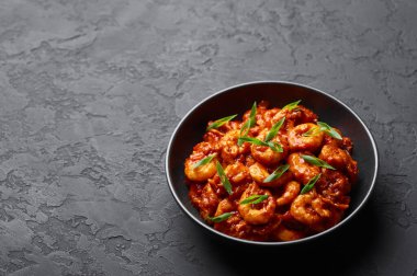 Schezwan Karidesleri siyah kasede, arka planda. Schezwan Karidesleri, Schezwan Sosu 'nda kızartılmış karides ve karidesli Hint-Çin mutfağı köri yemeği..