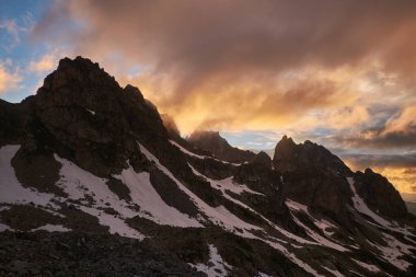 Dağlarda gün batımı. Karlı kayaların silueti dramatik bulutlu gökyüzünün altında. Sozarukova Tepesi, Kafkas Dağları Karachay-Çerkessia, Rusya.