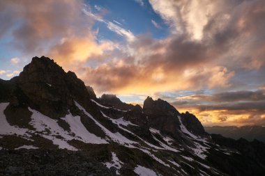 Dağlarda sersemletici bir gün batımı. Karlı kayaların silueti dramatik bulutlu gökyüzünün altında. Sozarukova Tepesi, Kafkas Dağları Karachay-Çerkessia, Rusya.