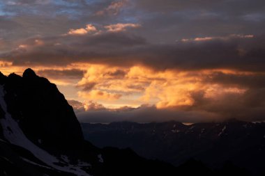 Dağlarda gün batımı bulutlu. Karlı kayaların silueti dramatik bulutlu gökyüzünün altında. Karachay-Çerkessia 'daki Kafkas Dağları, Rusya.