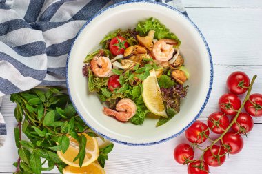 Beyaz ahşap masa üstünde nane ve limon ile süslenmiş deniz ürünleri salatası. Karidesli salata, midye ve kalamar..
