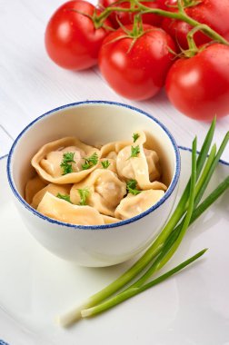 Beyaz ahşap masada maydanozlu ve soğanlı hamur tatlısı. Pelmeni - içinde kıyma olan geleneksel Rus yemek hamuru. Domateslerle süslenmiş.