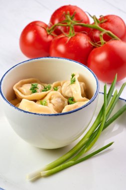 Beyaz ahşap masada maydanozlu ve soğanlı hamur tatlısı. Pelmeni - içinde kıyma olan geleneksel Rus yemek hamuru. Domateslerle süslenmiş.