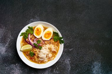 Mohinga siyah arka planda, beyaz tabakta. Mohinga, kedibalıklı, pilav erişteli, tavuk yumurtalı ve limonlu bir burma balık çorbası. Boşluğu sağda kopyala