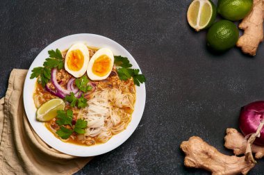 Mohinga siyah arka planda, beyaz tabakta. Mohinga, kedibalıklı, pilav erişteli, tavuk yumurtalı ve limonlu bir burma balık çorbası. Boşluğu sağda kopyala