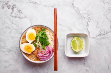 Mohinga beyaz mermer arka planda. Mohinga, kedibalıklı, pilav erişteli, tavuk yumurtalı ve limonlu bir balık çorbası..