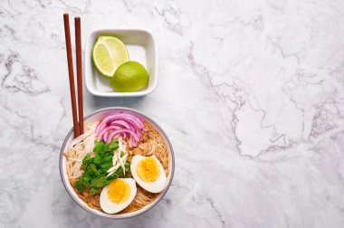 Mohinga beyaz mermer arka planda. Mohinga, kedibalıklı, pilav erişteli, tavuk yumurtalı ve limonlu bir burma balık çorbası. Boşluğu kopyala