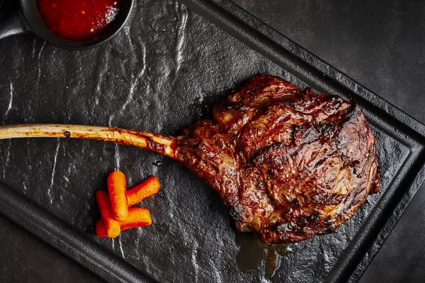 large beef tomahawk steak with sauce at black stone background garnished with french fries