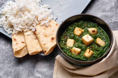 Palak Paneer şapkası ve gri beton arka planda basmati pirinci. Palak paneer ya da yeşil paneer, ıspanak ve paneer peynirinin Hint mutfağından yapılan bir yemektir. Boşluğu kopyala
