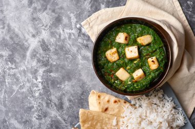 Palak Paneer şapkası ve gri beton arka planda basmati pirinci. Palak paneer ya da yeşil paneer, ıspanak ve paneer peynirinin Hint mutfağından yapılan bir yemektir. Boşluğu kopyala