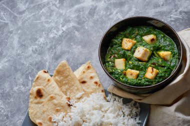 Palak Paneer şapkası ve gri beton arka planda basmati pirinci. Palak paneer ya da yeşil paneer, ıspanak ve paneer peynirinin Hint mutfağından yapılan bir yemektir. Boşluğu kopyala
