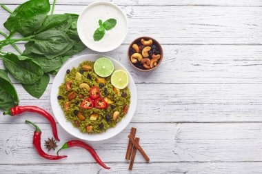 Palak Paneer Biryani and Raita at white wooden background with decor. Palak Paneer Biryani is vegetarian indian cuisine dish with spinach, paneer, basmati rice, spices, nuts and raisins. Copy Space