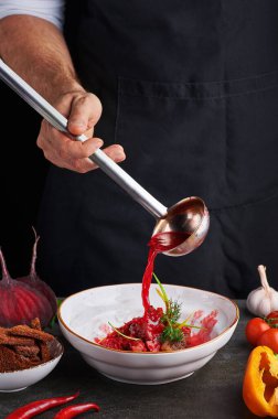 chef cook pours red soup borsch by ladle. Ukrainian and russian cuisine concept. vertical. Copy space