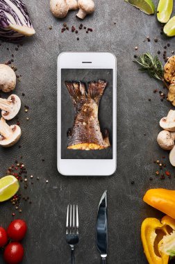 creative food concept with roasted fish tail in smartphone display. restaurant delivery concept. Gourmet cuisine. Vertical