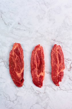 raw marbled beef steaks at white marble background. copy space. vertical