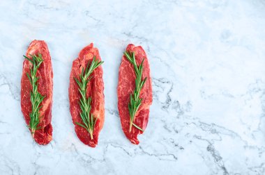 raw marbled beef steaks with green rosemary branch at white marble background. copy space
