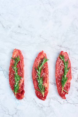 raw marbled beef steaks with green rosemary branch and sea salt at white marble background. Copy space. vertical